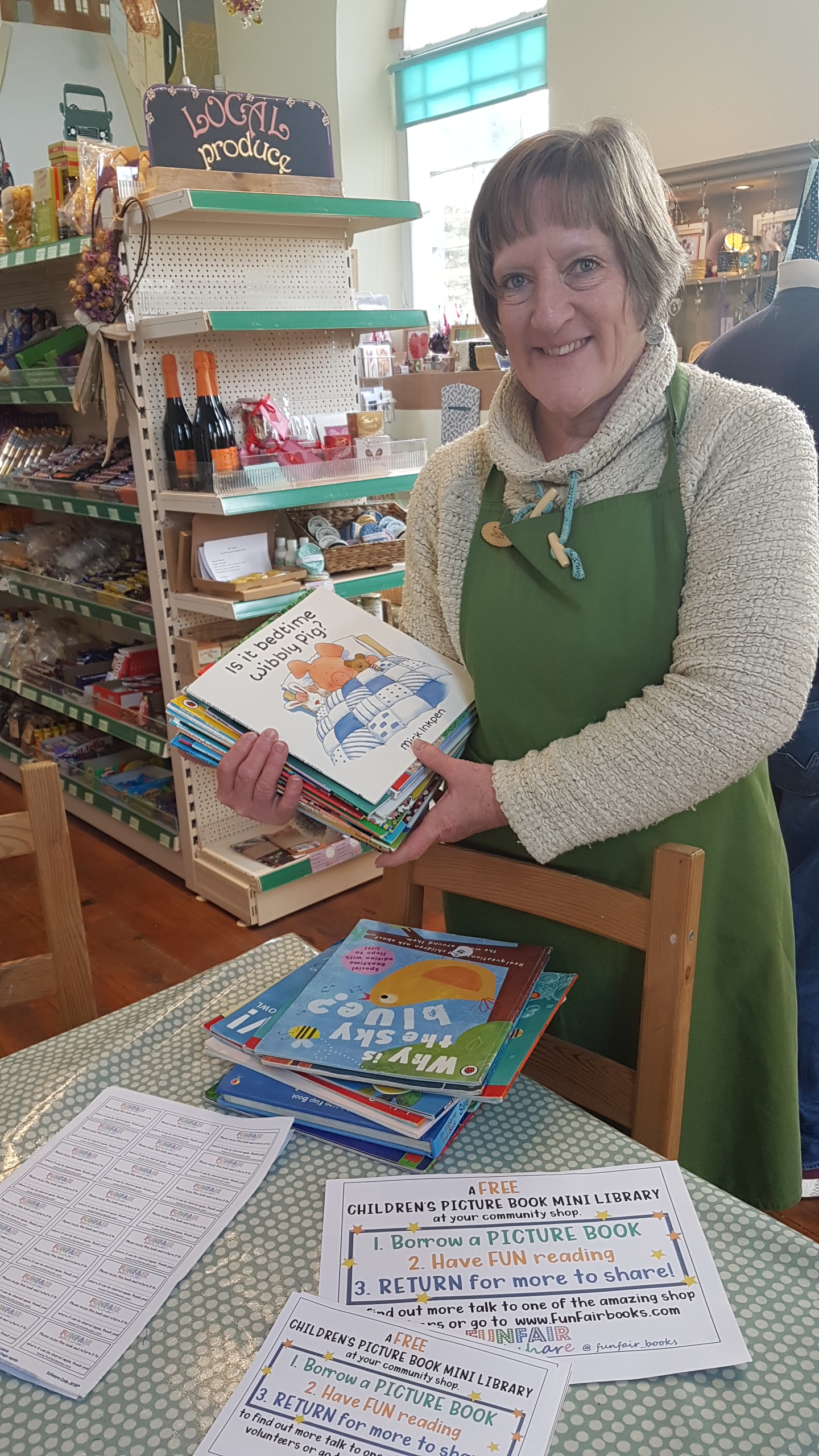 community shop manager holding up book donations received from us